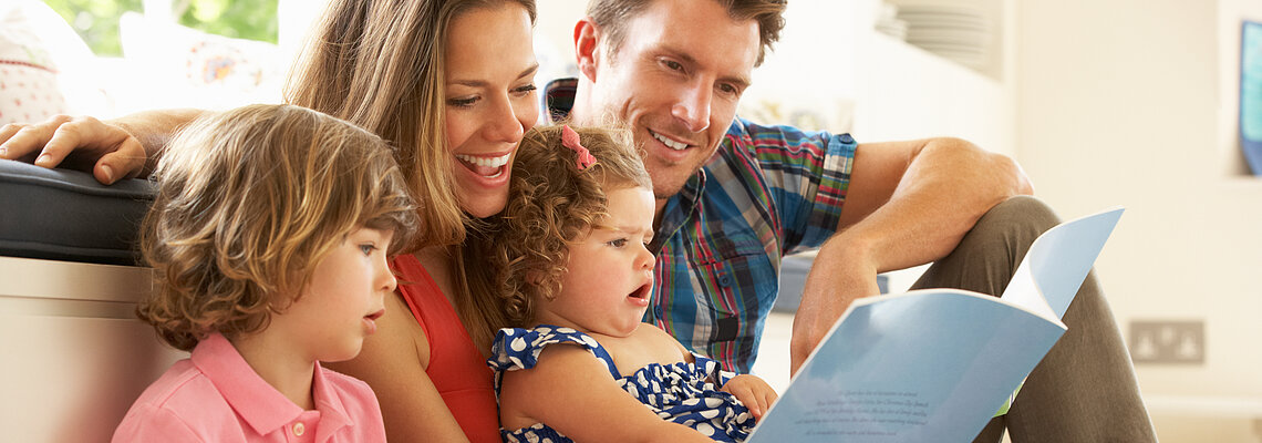 Parents Sitting With Children Reading Story Indoors