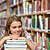 Happy student sitting on library floor leaning on pile of books in college