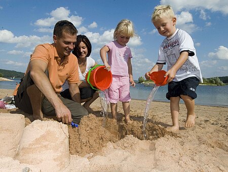 Eine vierköpfige Familie spielt am Strand des Brombachsees in Ramsberg. Die zwei Kinder erfreuen sich am sandeln und genießen die Zeit.