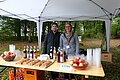 Zwei Mitarbeiterinnen des Landratsamtes kümmern sich um die Genussstation. Es werden Äpfel, Müsliriegel und Getränke angeboten. Sei stehen unter einem Pavillon im Wald.