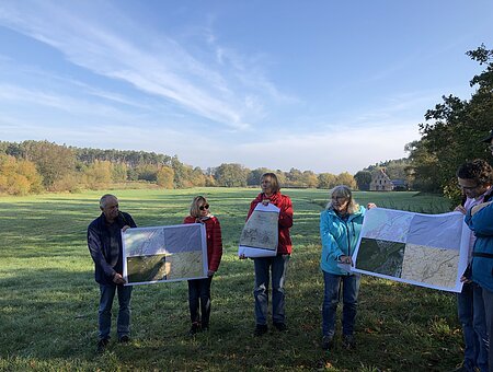 Von fünf Teilnehmern werden große Karten gehalten, damit der Teilnehmerkreis diese sehen kann. Sie stehen auf einer grünen Wiese.