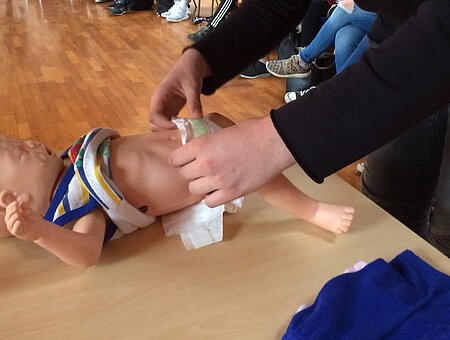 Zu sehen sind Hände die eine Babypuppe wickeln.