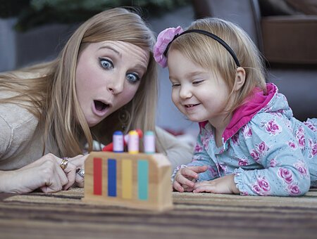 Happy mom teaching her baby girl the colors with a wooden toy