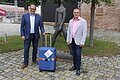 Landrat Manuel Westphal steht mit Bürgermeister Rampe zusammen. Vor Ihnen steht ein blauer Reisekoffer.