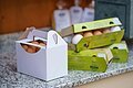 Ein weißer quadratischer Karton sowie drei grüne Schachteln gefüllt mit weißen und braunen Eiern steht auf einem Marmortisch