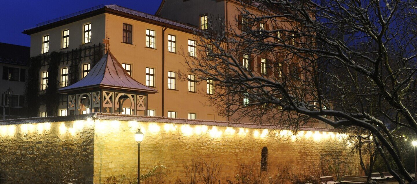 Ein Stadtschloss leuchtet aus allen Fenstern in der winterlichen Zeit und ist umgeben von Schnee.