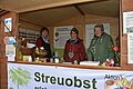 Drei Frauen stehen in einer Hütte und verkaufen augenscheinlich etwas. Alle drei lächeln. Im Vordergrund erkennt man auf einem Banner das Wort Streuobst.