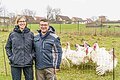 Eine blonde Frau und ihr Mann stehen vor dem Gehege, im Hintergrund die weißen Puten