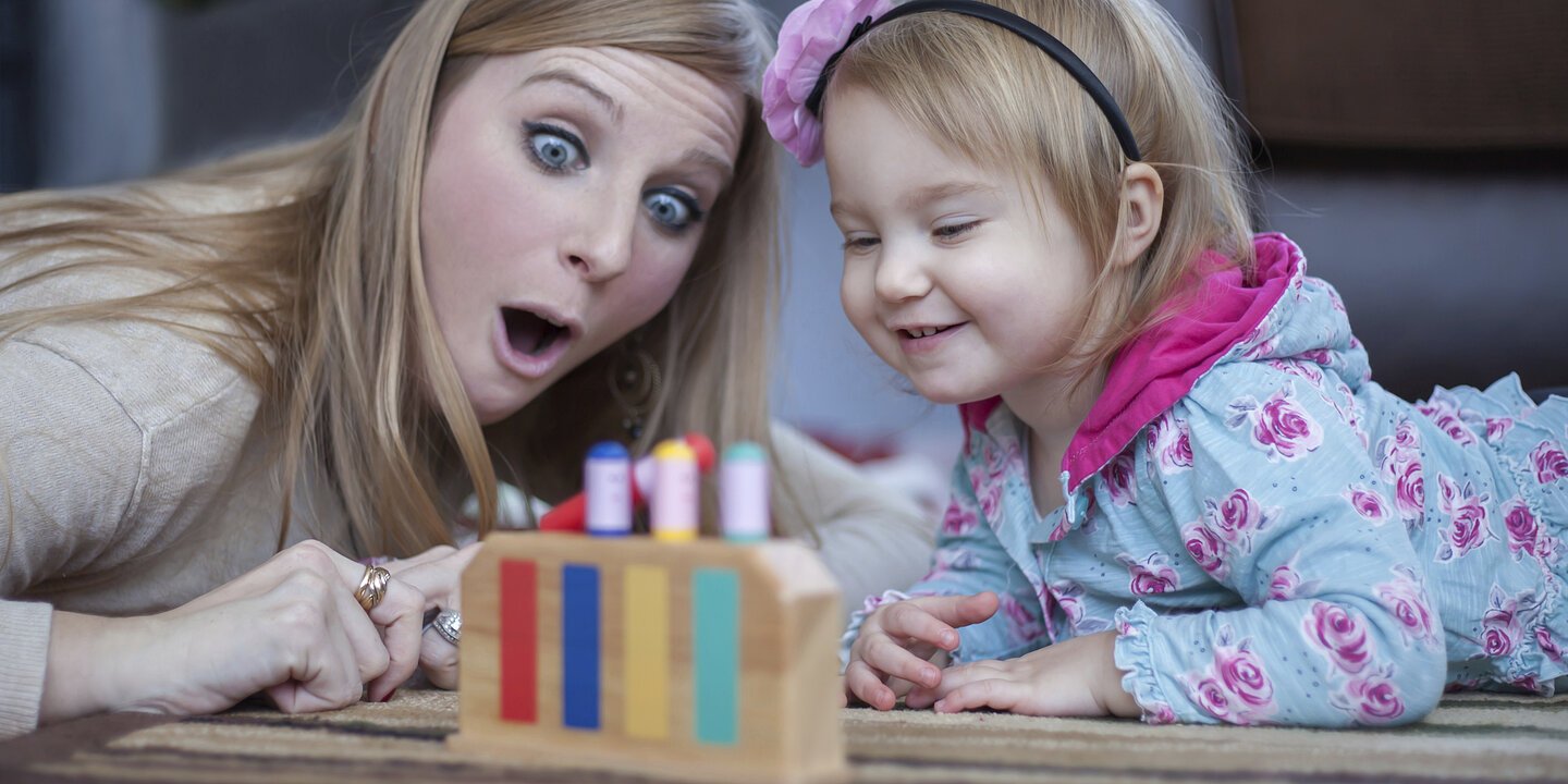 Happy mom teaching her baby girl the colors with a wooden toy