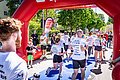 Läuferinnen und Läufer in weißen Trikots laufen gemeinsam ins Ziel ein. Das Ziel ist mit einem roten Torbogen und einem blauen Teppich gekennzeichnet.