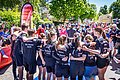 Junge Menschen stehen im Halbkreis mit schwarzen Shirts und umarmen sich. Sie werden dabei fotografiert.