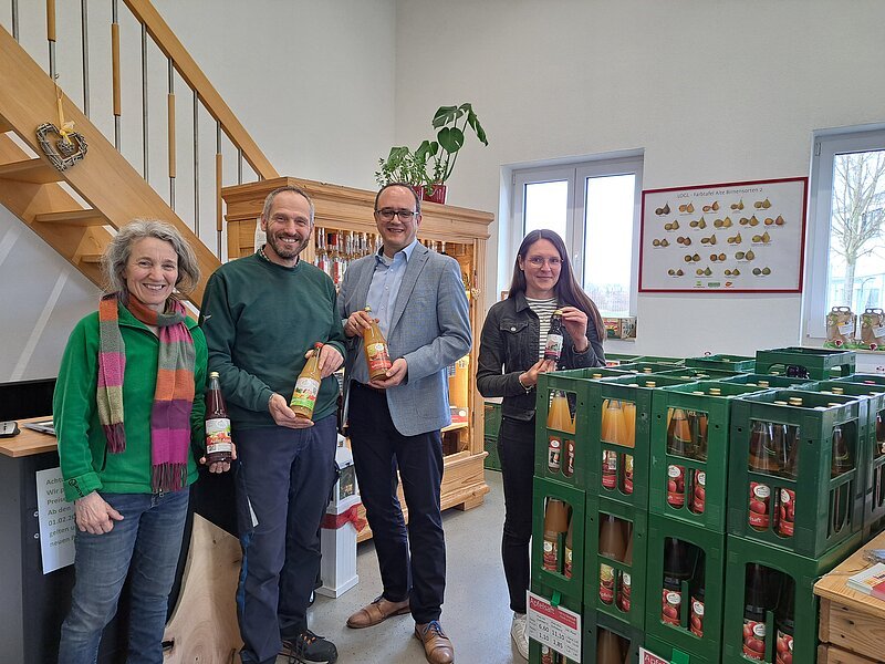 Es sind vier Personen zu sehen, welche die Produkte der Mosterei in den Händen halten und für ein Gruppenbild in die Kamera schauen.