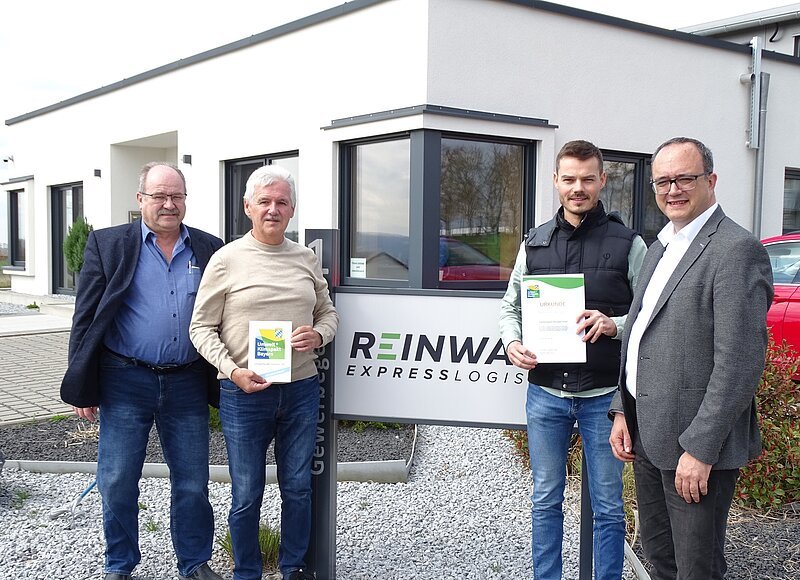 Ein Gruppe von Männern präsentiert die Urkunde des Umwelt- und Klimapakt Bayern und blickt dabei für ein Gruppenbild in die Kamera.