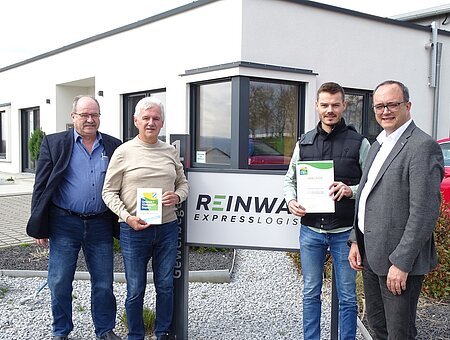 Ein Gruppe von Männern präsentiert die Urkunde des Umwelt- und Klimapakt Bayern und blickt dabei für ein Gruppenbild in die Kamera.