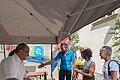Am Infostand verteilt Landrat Manuel Westphal Gutscheine an drei Teilnehmer, die Radklamotten tragen.