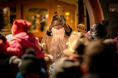 Ein Mann, der als Pelzmärtel verkleidet ist, steht vor einer Gruppe Kinder und verteilt Geschenke.