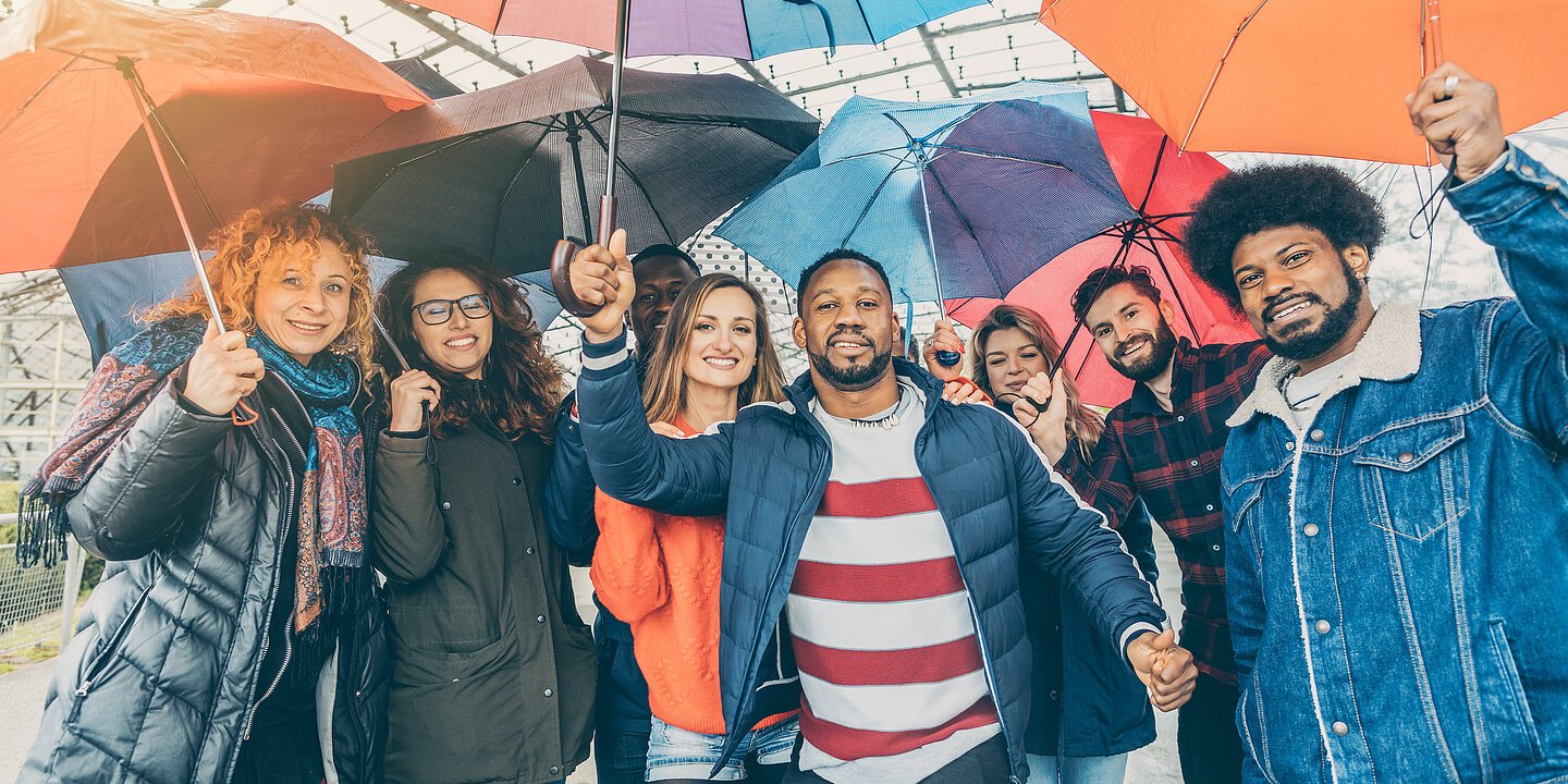 Eine Gruppe Menschen die unter Regenschirmen stehen.