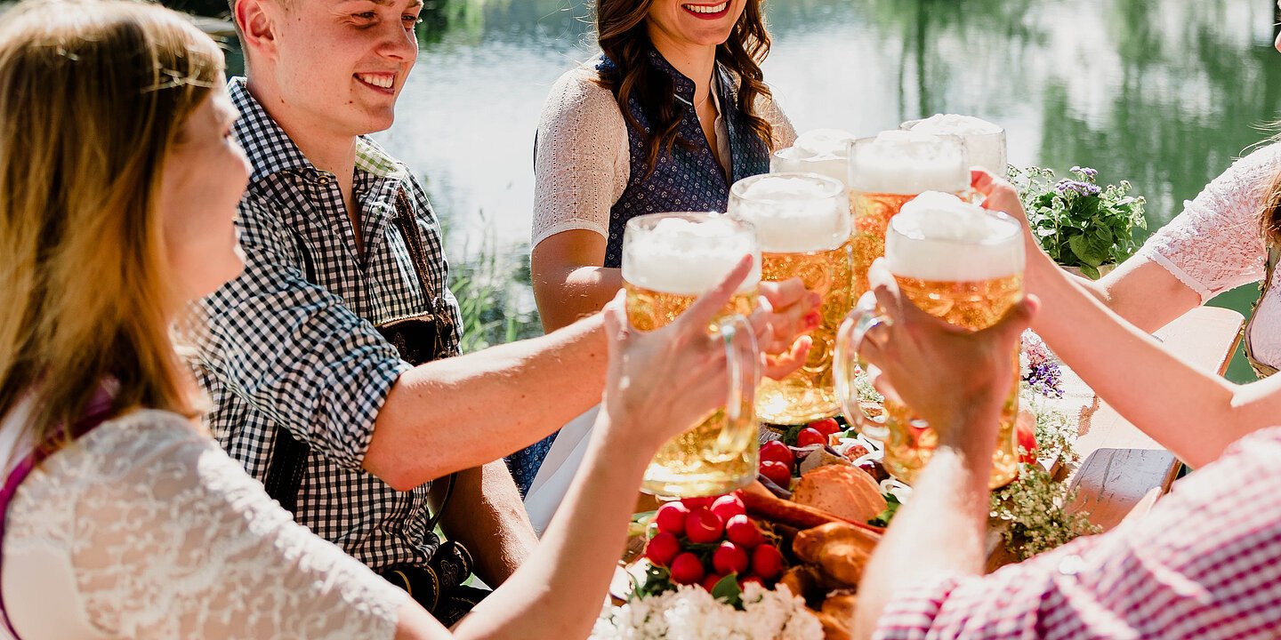 Frauen und Männer in Tracht stoßen mit einem Maßkrug Bier an. Im Hintergrund der Fluss Altmühl.