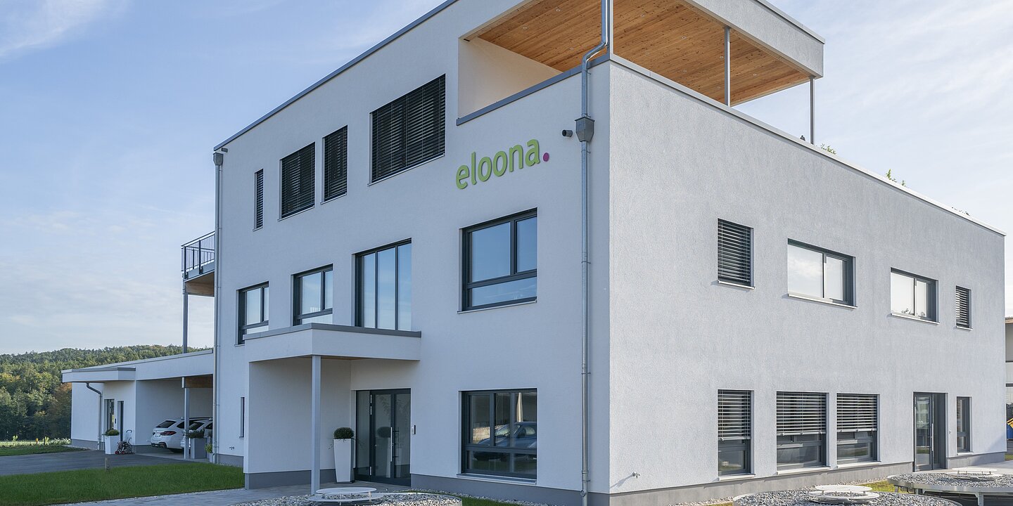 Es ist das weiße Betriebsgebäude der Eloona GmbH aus Pleinfeld zu sehen.