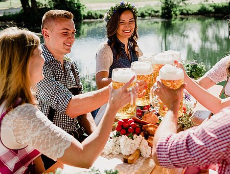 Frauen und Männer in Tracht stoßen mit einem Maßkrug Bier an. Im Hintergrund der Fluss Altmühl.