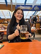 Eine junge braunhaarige Frau im Dirndl sitzt am Biertisch - in der Hand hält sie einen Maßkrug.