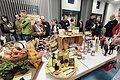 Ein großer Tisch mit verschiedenen regionalen Produkten, um den Tisch stehen viele Leute und unterhalten sich.