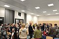 In einem Raum stehen viele Menschen, die sich zwischen den Stühlen miteinander beim Speed-Dating unterhalten.