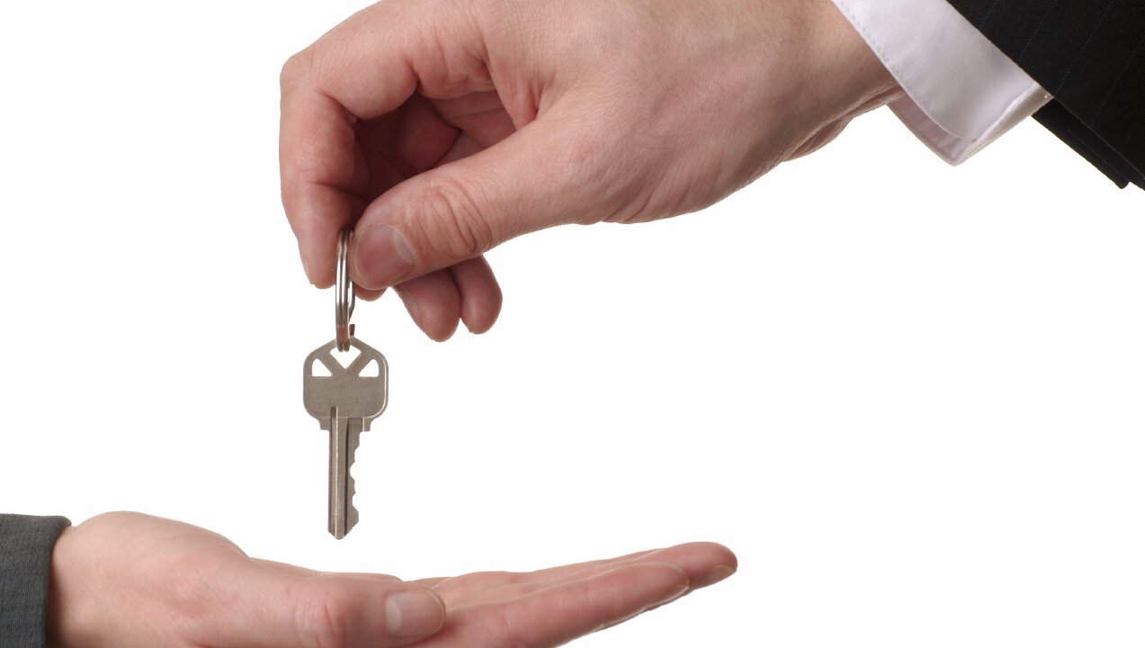 Businessman handing a key over to a businesswoman.  Isolated on white
