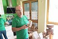 Ein Mann im grünen T-Shirt steht in einem Verkaufsraum, hat ein Glas mit Getreide in der Hand und erklärt seine Produkte, die vor ihm in Papiertüten stehen